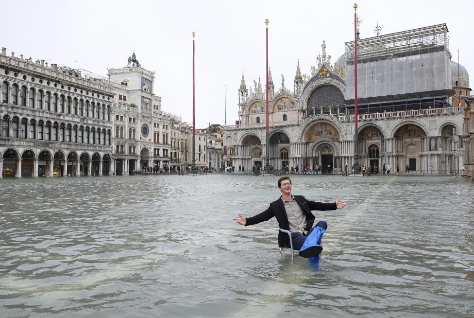 a man poses in a flooded st. mark's square during a period of seasonal high water in venice