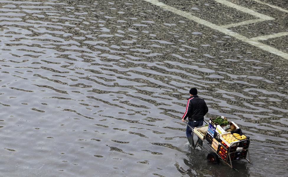 a man pulls a cart carrying fruits and vegetables through a flooded st. mark's square during a period of seasonal high water in venice