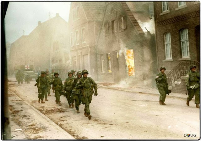 Troops of the 17th U.S. Airborne Division, First Allied Airborne Army, march past a blazing building in Appelhülsen, Germany, as they advance toward the city of Münster, nine miles to the northeast. First Allied Airborne Army troops had landed east of the Rhine river on March 24th 1945. (Colorized by Doug)