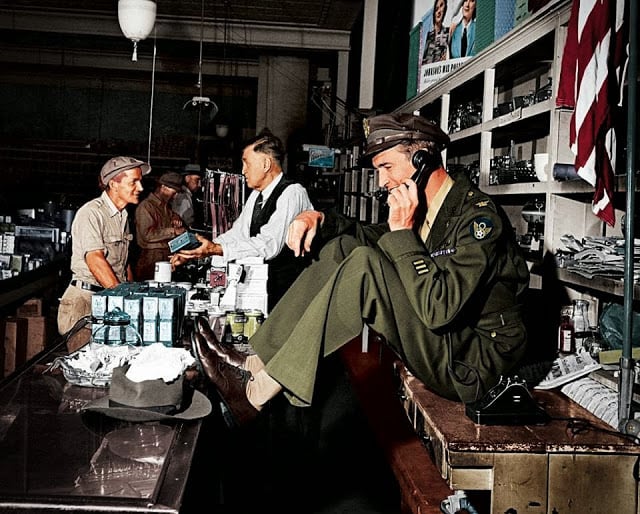 While his father chats with a customer at the hardware store, a uniformed Jimmy Stewart sets up a date to go fishing,1945. (Colorized by John Gulizia from America)